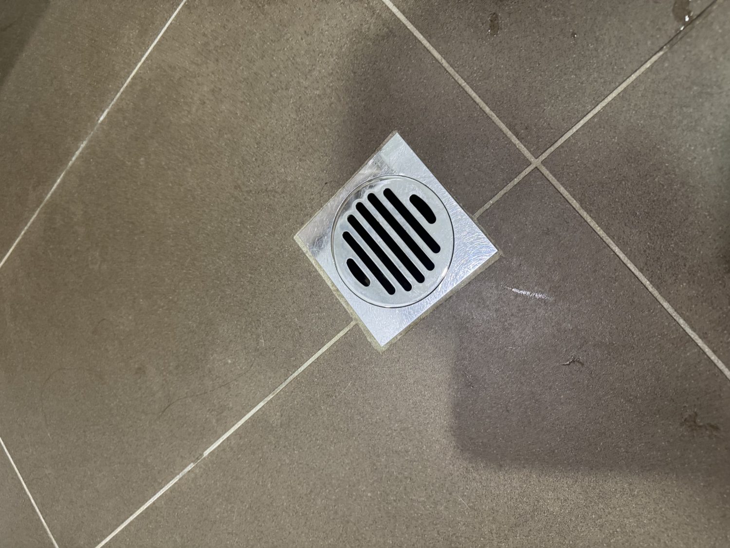 Square stainless steel grated floor waste set into a tiled bathroom floor
