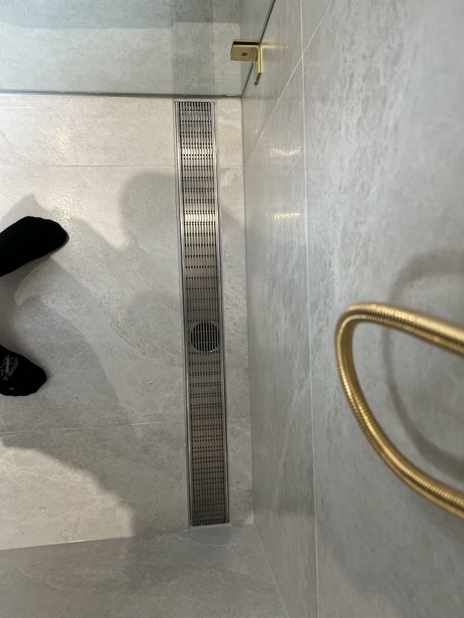 Stainless steel grated strip drain running along the wall of a tiled shower