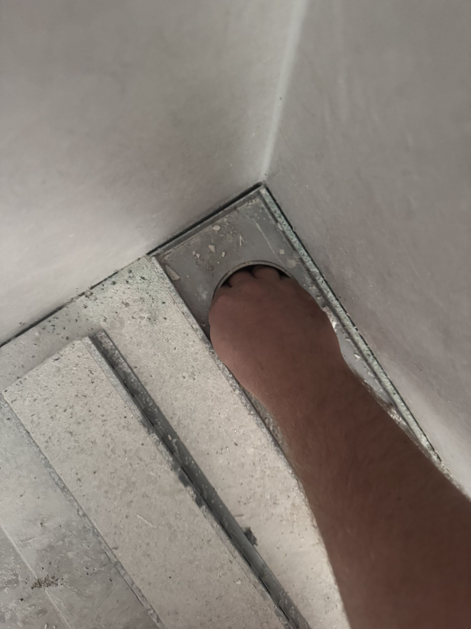 A hand being pushed into a shower drain outlet that is too small to fit past the knuckles