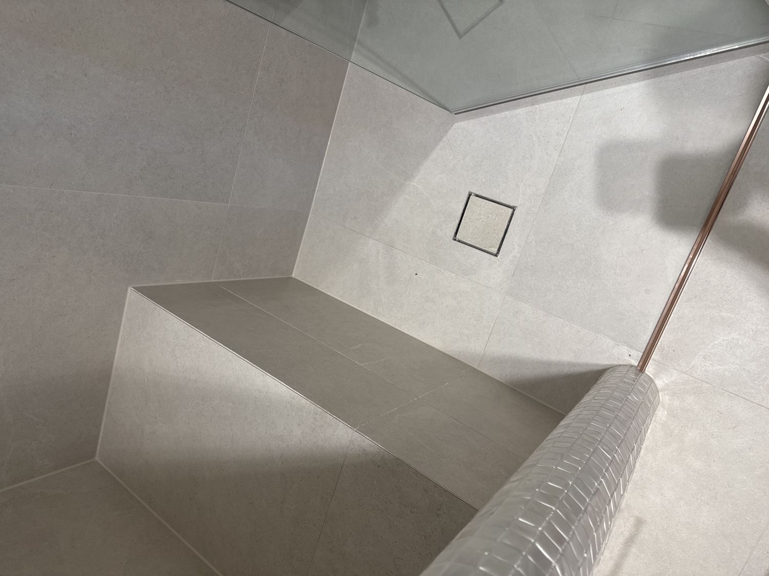Tile insert point drain in a shower floor with the floor tile set into the drain and two thin slots showing