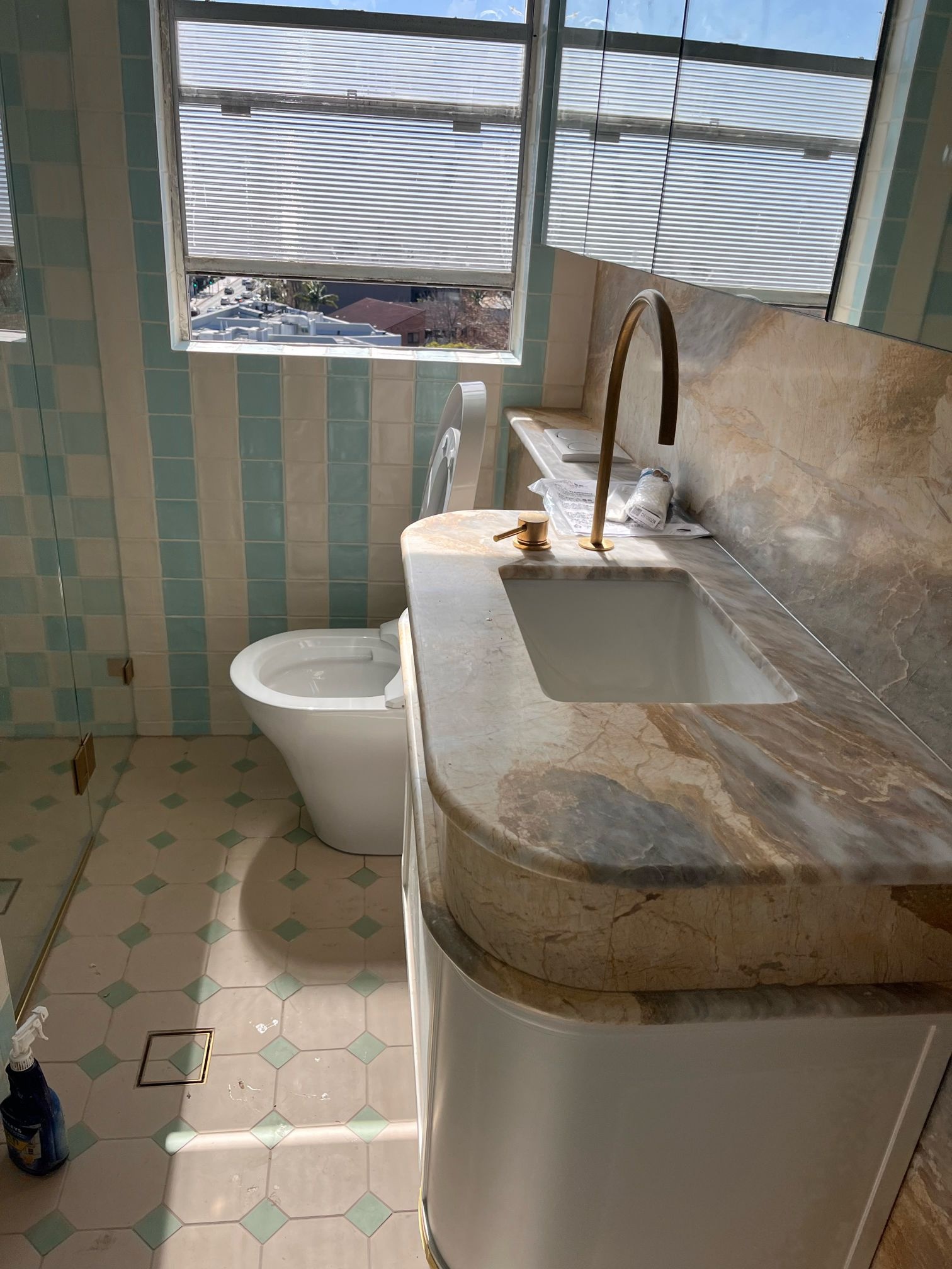 Marble bathroom vanity with a white basin, brass tap and toilet beside mint and white tiles