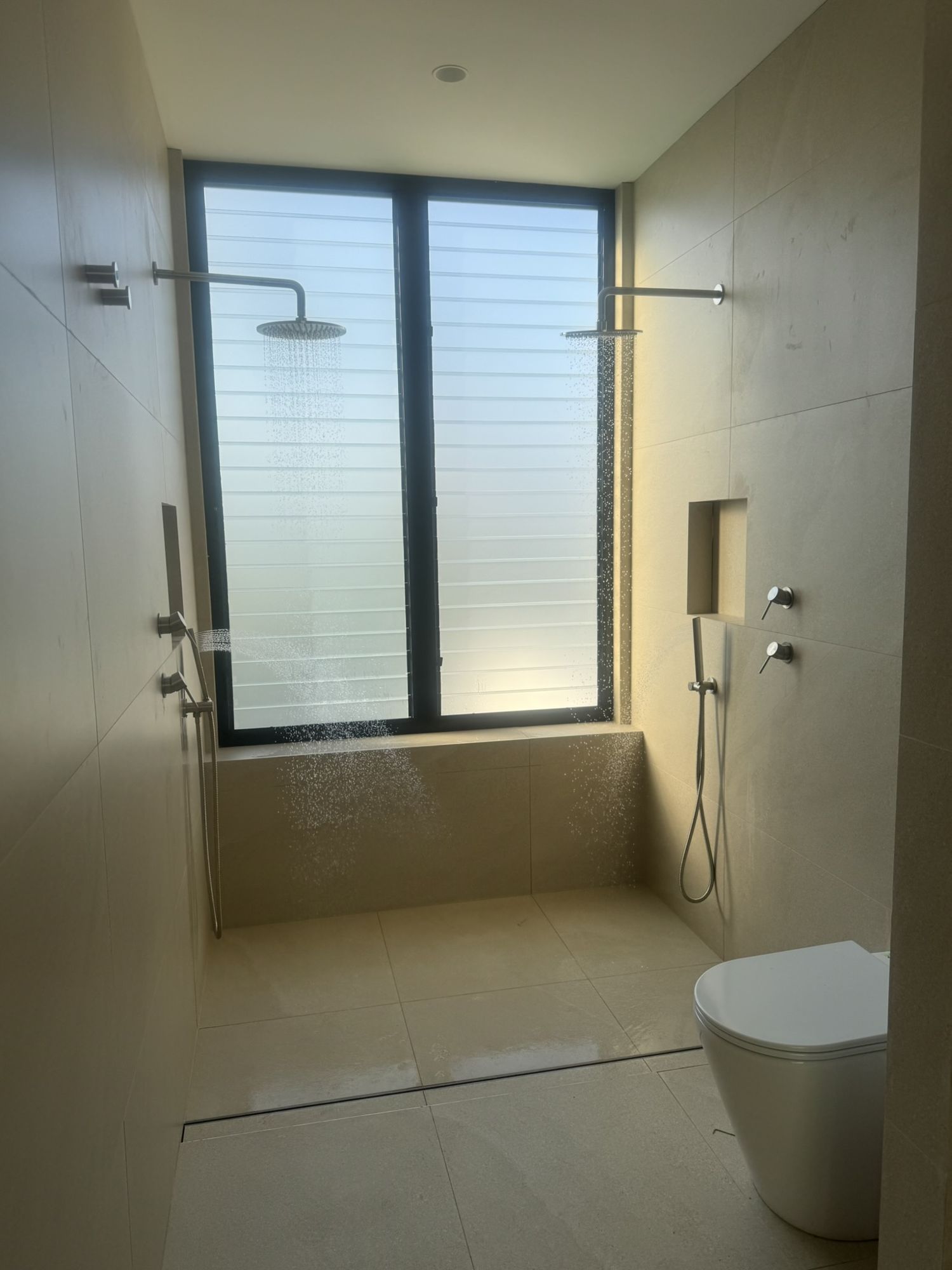 Strip drain set across a shower entry with a step-down in the tiled floor