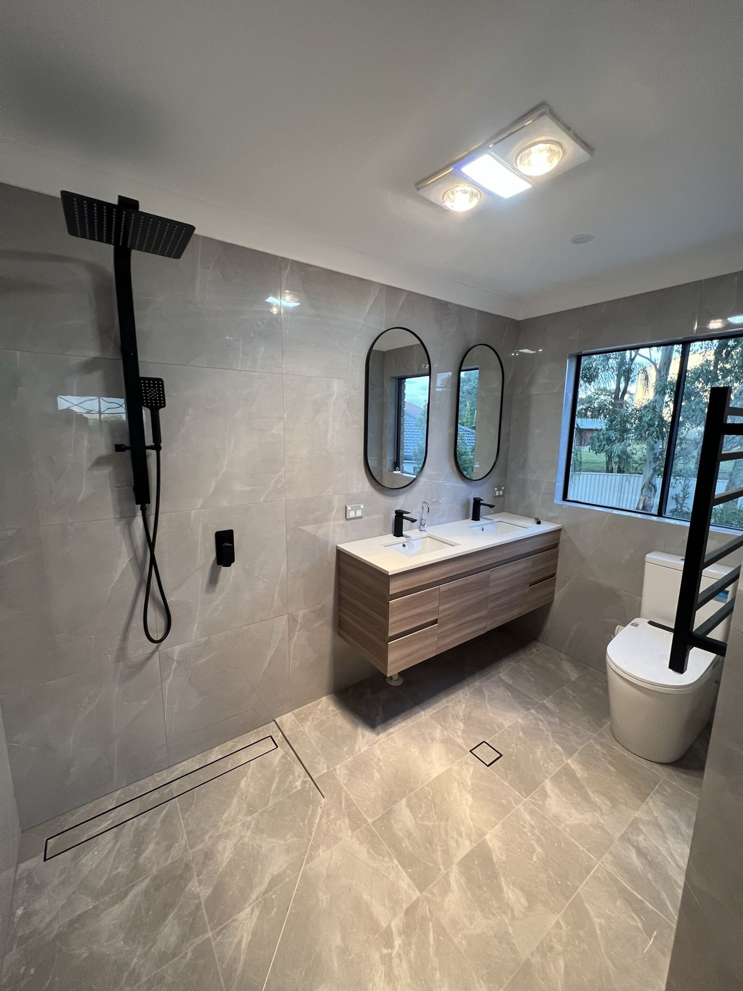 Modern bathroom with a tile insert strip drain with a black inner set into the shower floor, matched to black tapware