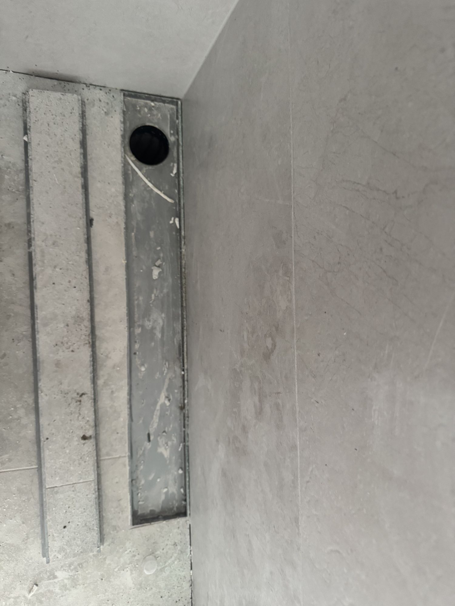 Channel drain outlet jammed hard into the corner of a tiled bathroom floor