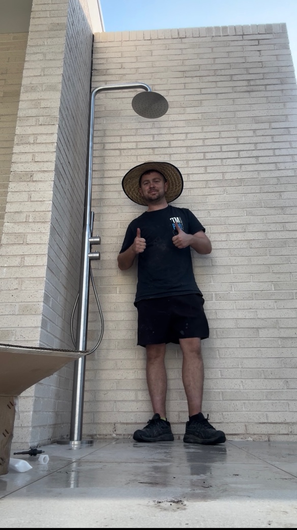 TM Pro plumber standing beside a tall outdoor shower he installed against a brick wall