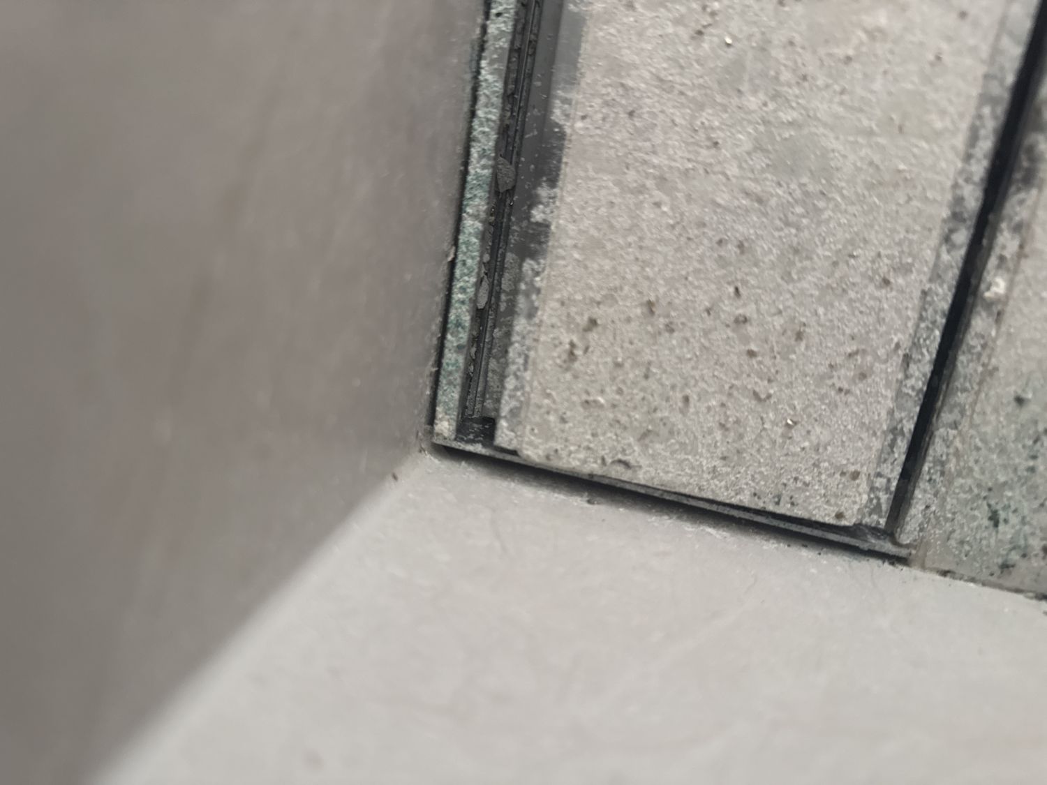 Tile insert drain set too tight into a tiled corner with a dirty grout line and no room to silicone