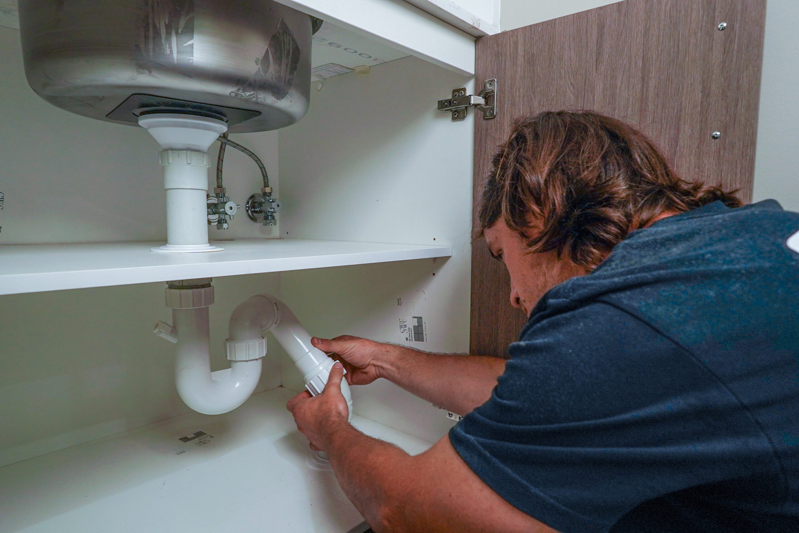 TM Pro plumber checking the waste pipe under a kitchen sink for leaks