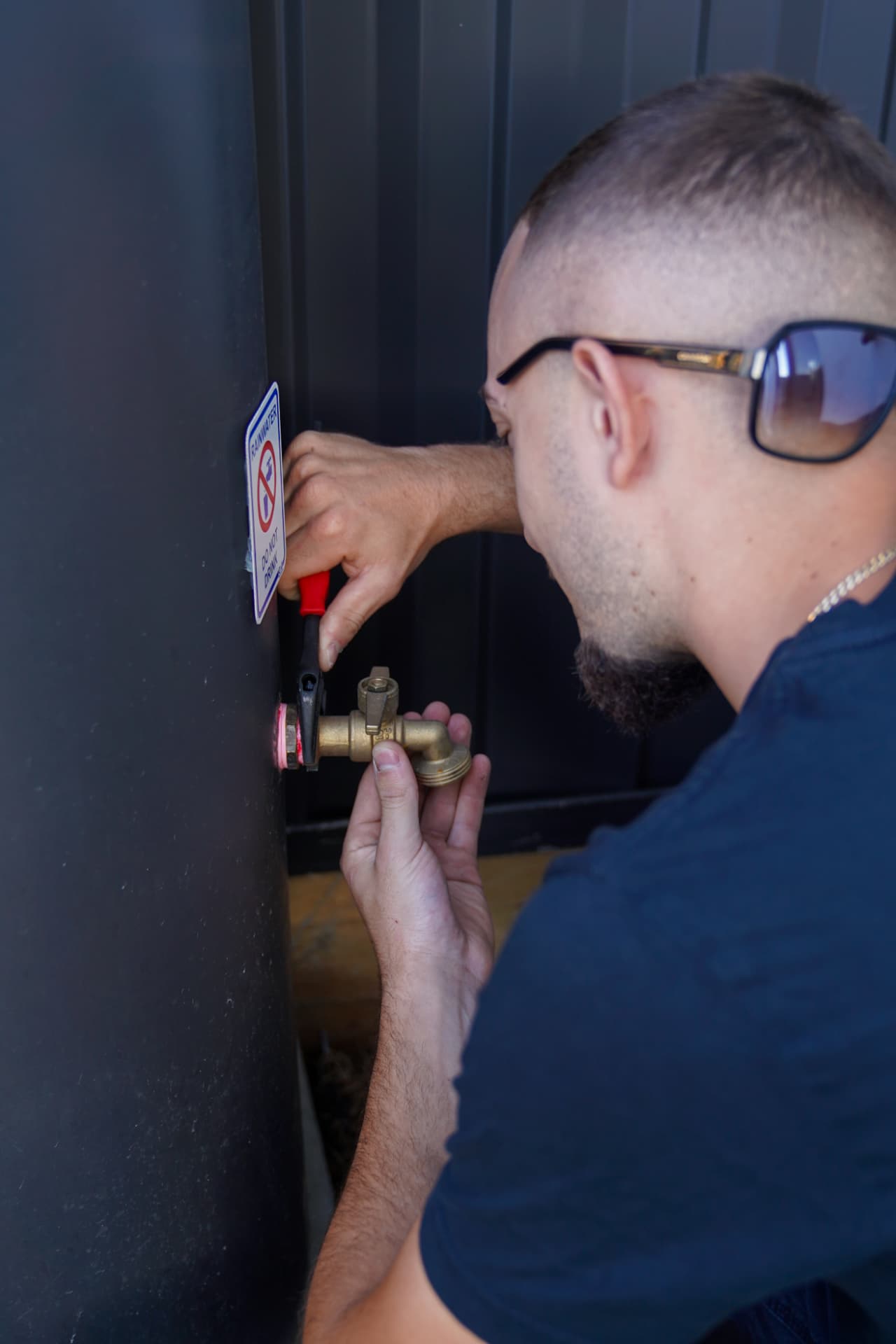 Plumber fitting a brass tap to a rainwater tank marked Do Not Drink